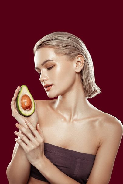 Blonde-haired model wearing dark top holding avocado - Photo, Image
