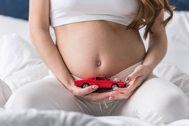 Vágott piros játékautó gazdaság terhes nő képe - Fotó, kép