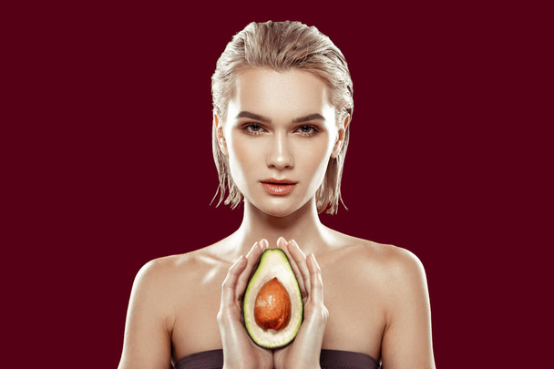 Модель тримає авокадо в руках, стоячи біля червоної стіни
 - Фото, зображення