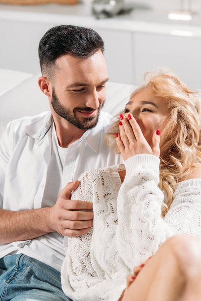Blonde girl laughing while embracing with boyfriend at home - Photo, Image