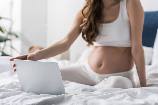 Cropped view of pregnant woman sitting on bed and using laptop - Fotografie, Obrázek