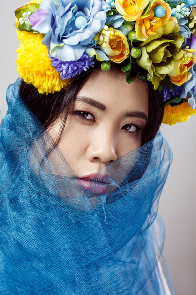 portrait of sensual asian beautiful woman with floral hat and blue veil on light grey background, close-up  - Fotografie, Obrázek
