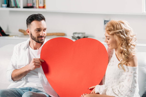 Couple romantique assis sur un canapé avec un grand cœur rouge
 - Photo, image