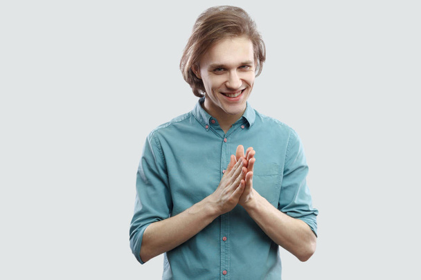 Portrait of cunning long haired blonde man in blue shirt standing and looking at camera with bitchy plan  - Photo, image
