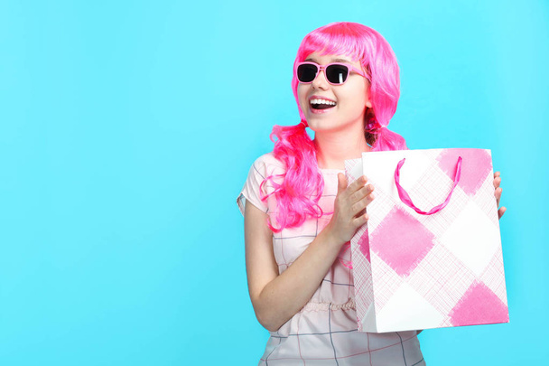 Όμορφη κοπέλα χαμογελαστή με φωτεινά ροζ μαλλιά στο φόρεμα με τσάντα για ψώνια σε μπλε φόντο. Πώληση έννοια, ψώνια. - Φωτογραφία, εικόνα