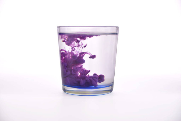 Vidrio con agua sobre fondo blanco con pintura púrpura
. - Foto, Imagen