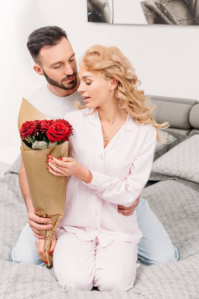 Hombre presentando flores a su novia mientras está sentado en la cama
 - Foto, imagen