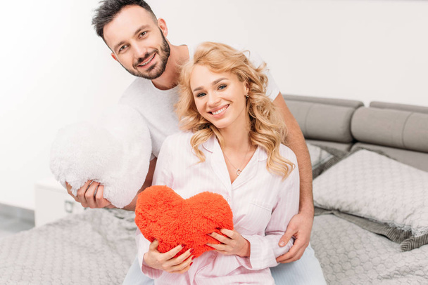 Excited couple holding toy hearts while sitting on bed - Foto, immagini