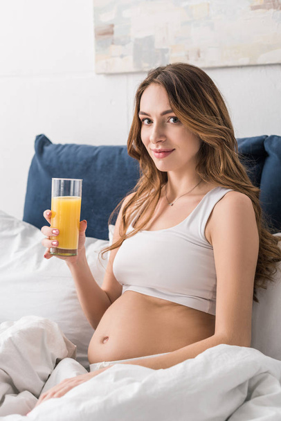 Pregnant young woman drinking juice in bed - 写真・画像