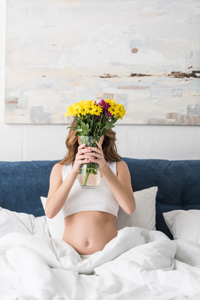 Femme enceinte assise dans son lit et tenant un vase avec des fleurs
 - Photo, image