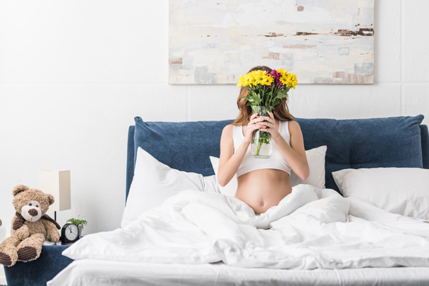 Pregnant woman lying in bed and holding vase with fresh flowers - Foto, Bild