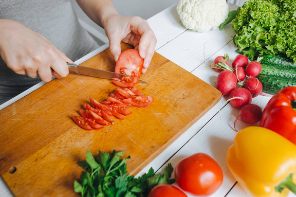 Woman hands cutting fresh red tomato on wooden board closeup. White table background. - Photo, Image