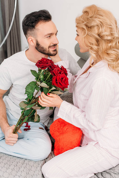 Щаслива пара позує з іграшковим серцем і червоними трояндами
 - Фото, зображення