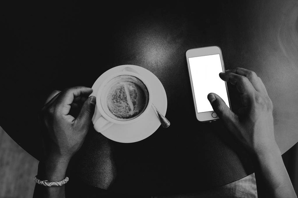 Closeup view of male hands touching mobile phone.African man using smartphone while sitting at the wooden table.Empty white blank copy space screen for your information.Mockup.Black and white. - Foto, Bild