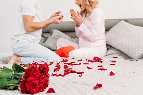 abgeschnittene Ansicht eines Mannes, der auf dem Bett sitzt und Freundin einen Heiratsantrag macht - Foto, Bild