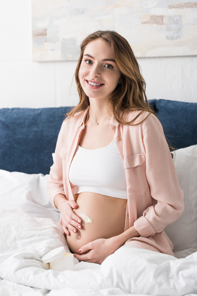 Smiling pregnant woman applying cream on belly - Fotoğraf, Görsel