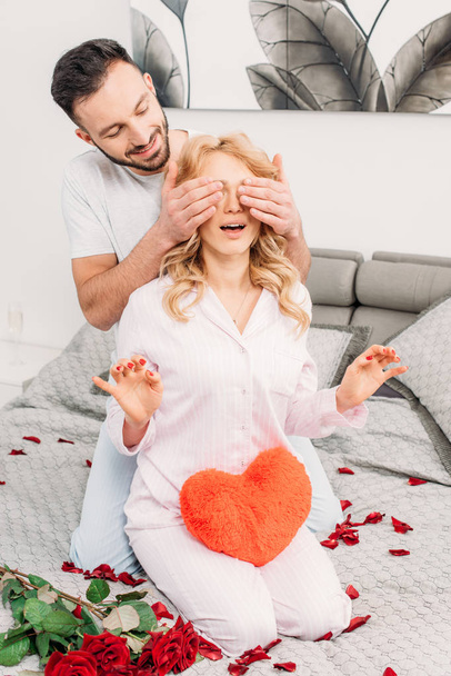 Man sitting on bed with roses and covering girlfriend's eyes - Foto, imagen