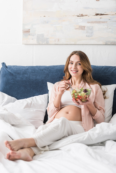 Laughing pregnant woman eating salad in bed - Foto, Bild