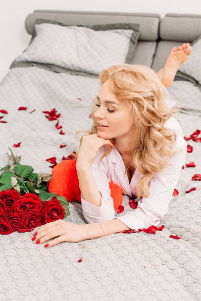 Stunning young woman lying on bed with roses - Foto, Imagen