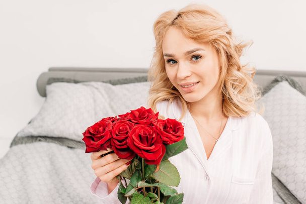 Cheerful blonde girl posing with roses in bedroom - Fotó, kép