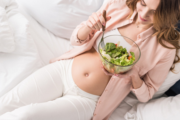 Vue partielle de la jeune femme enceinte mangeant de la salade au lit
 - Photo, image