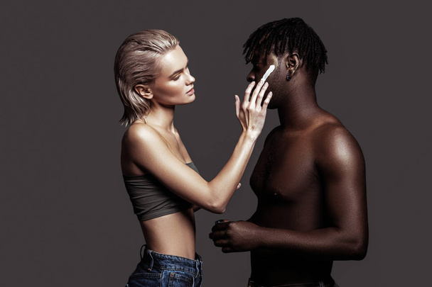 Blonde-haired model putting some cream on African-American man - Foto, immagini