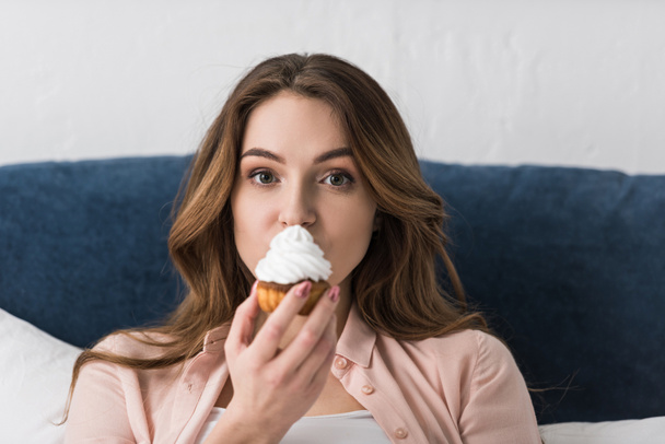 Brunette beautiful woman eating cupcake and looking at camera - Photo, Image