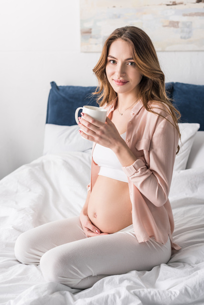 schöne schwangere Frau sitzt mit Kaffeetasse im Bett - Foto, Bild