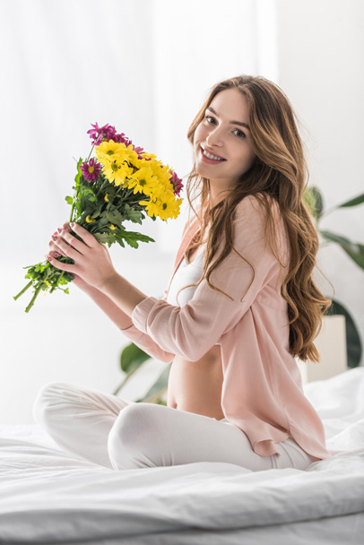 Boldog terhes nő ül az ágyon, virágok - Fotó, kép