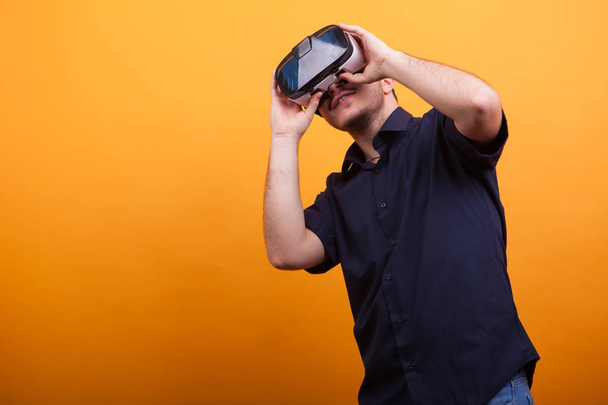 Young man in casual blue shirt with VR goggles over yellow background - Foto, immagini