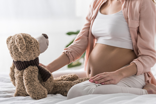 Rajatut näkymä raskaana oleva nainen istuu sängyllä lelu karhu
 - Valokuva, kuva