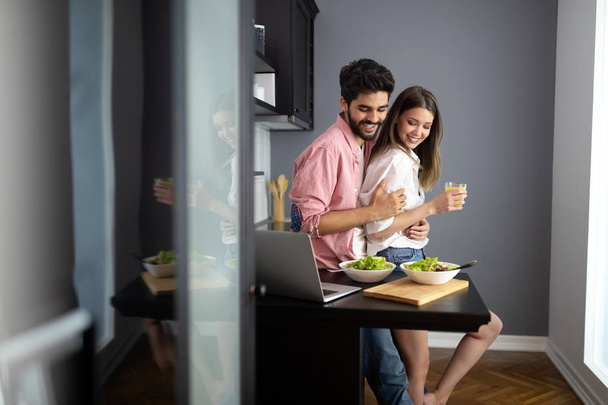 Beautiful young couple is talking and smiling while cooking healthy food in kitchen at home - Φωτογραφία, εικόνα