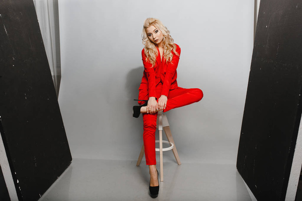 Young woman in the red suit sitting on the chair in the studio - Foto, Imagem