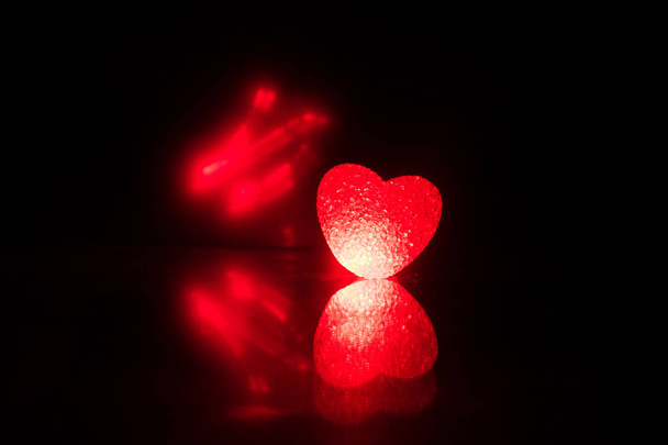 Mesa escura, conceito do dia dos namorados e amor coração forma vermelha com fundo bokeh, vazio para texto e colocação de produtos com espaço de cópia. Coração incandescente borrado sobre um fundo escuro com reflexão
 - Foto, Imagem