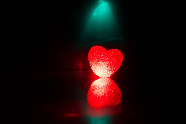 dunkler Tisch, Valentinstag Konzept und Liebe rote Form Herz mit Bokeh Hintergrund, leer für Text und Platzierung von Produkten mit Kopierraum. verschwommenes glühendes Herz auf dunklem Hintergrund mit Reflexion - Foto, Bild