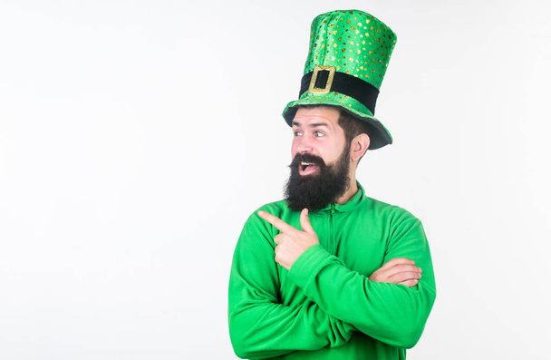 Pointing at something aside. Irish man with beard pointing his finger. Bearded man celebrating saint patricks day. Hipster in green leprechaun hat and costume. Happy saint patricks day, copy space - 写真・画像