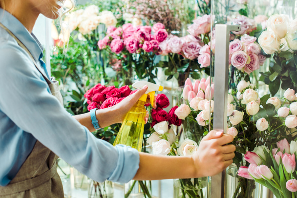 cropped view of female florist spraying flowers with spray bottle in flower shop - Photo, Image