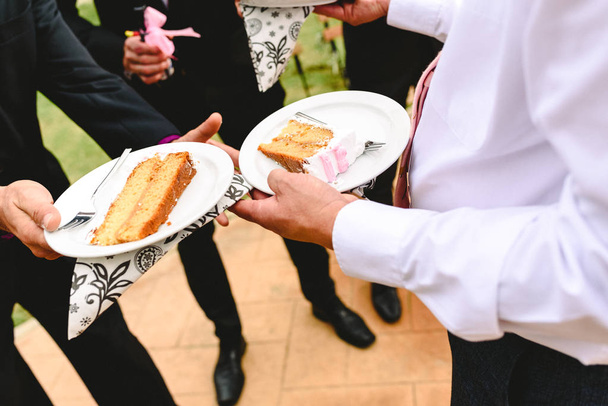 Sliced wedding cake delivered to the guests by the hand of a waiter. - Photo, Image