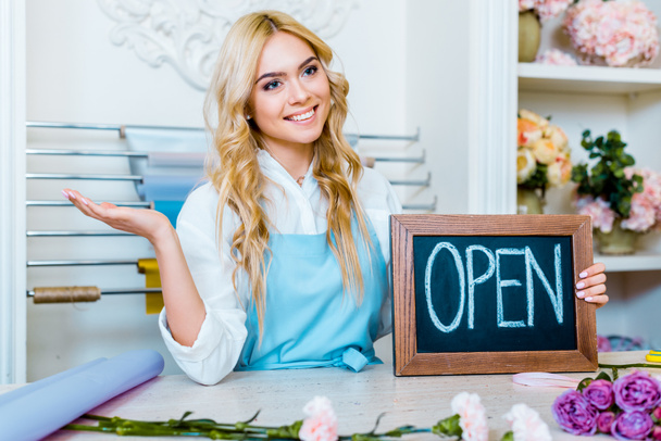 krásnou usměvavou samičí květ majitel obchodu pokynul rukou a držení tabuli s nápisem "otevřené"  - Fotografie, Obrázek