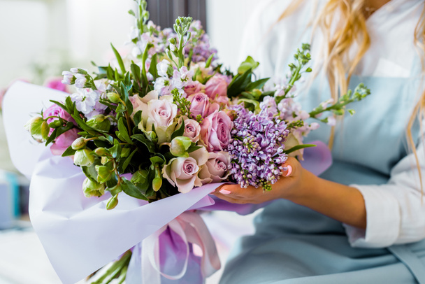 cropped view of female florist holding bouquet with lilac and roses in flower shop - Fotó, kép
