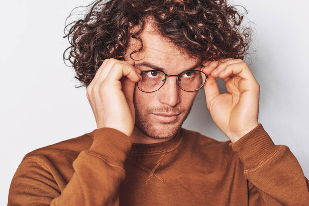Horizontal closeup portrait of serious young male with curly hair, wears round trendy spectacles, looking to at one side. Business man posing on white studio wall.  - Valokuva, kuva