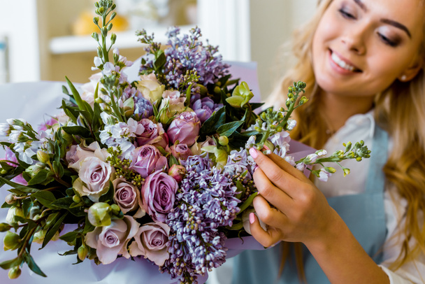 smiling female florist arranging bouquet with lilac and roses in flower shop - Photo, Image
