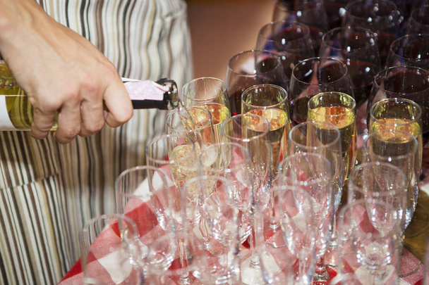 Πολλά ποτήρια με το αλκοόλ, λευκό γυαλιά κρασιού διέλευση ποτήρια κόκκινο κρασί. Μπουκάλι κρασί ρίχνει μια σειρά γυαλιών για γευσιγνωσία για υπηρεσία σε πάρτι και εκδηλώσεων. ποτήρια με κρασί γκρο πλαν πριν από κόμμα σε καφετέρια - Φωτογραφία, εικόνα