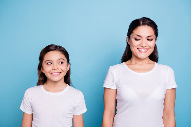 Close up photo amazing pretty two people brown haired mum and small daughter standing straight looking side each other cunning wearing white t-shirts isolated on bright blue background - Foto, Imagem