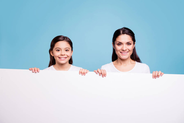 Close up photo pretty two people brown haired mum little daughter toothy beaming smile blank signboard poster in arms sale discount wearing white t-shirts isolated bright blue background - Photo, image