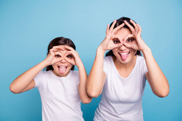 Close up photo beautiful two people brown haired mom little daughter best friends look through finger glasses specs okey symbol tongue out mouth wearing white t-shirts isolated bright blue background - Foto, afbeelding