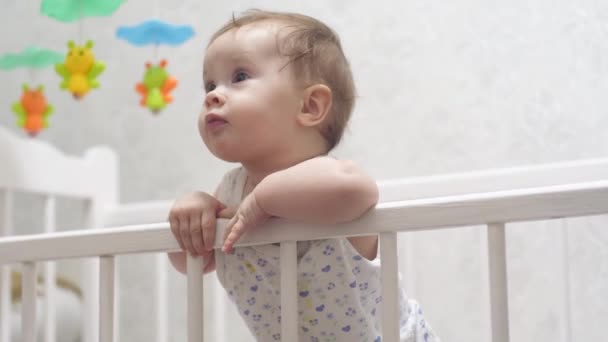 happy child stands on his feet in baby bed. baby laughs - Záběry, video