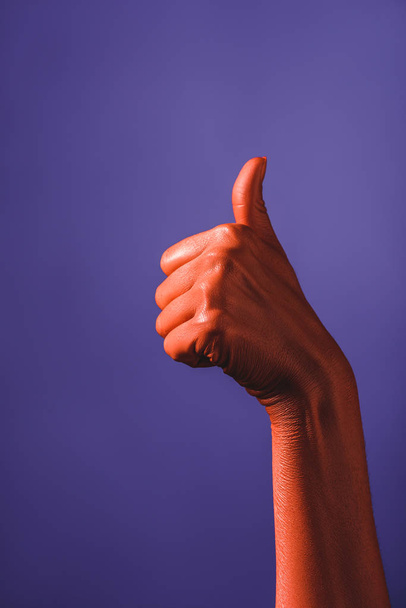 partial view of woman showing thumb up on coral colored hand on violet background, color of 2019 concept - Photo, Image