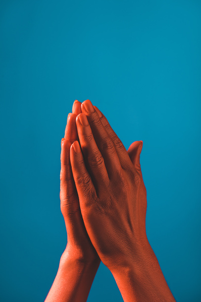 partial view of  woman showing pray sign by coral colored hands on blue background, color of 2019 concept - Fotografie, Obrázek