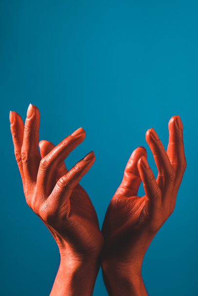 partial view of woman gesturing with coral colored hands on blue background, color of 2019 concept - Φωτογραφία, εικόνα